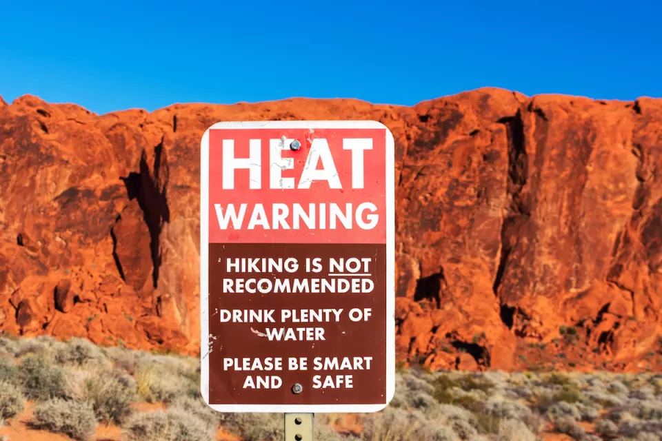 Extreme heat warning sign outdoors with red desert rock cliff in background.